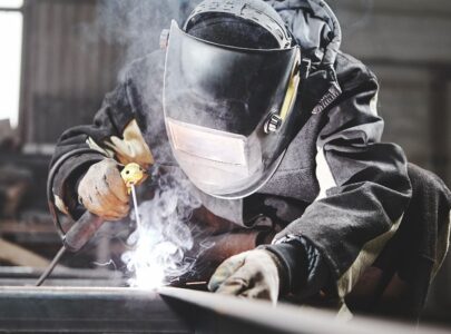 Welder working with welding on metal frames in an industrial plant